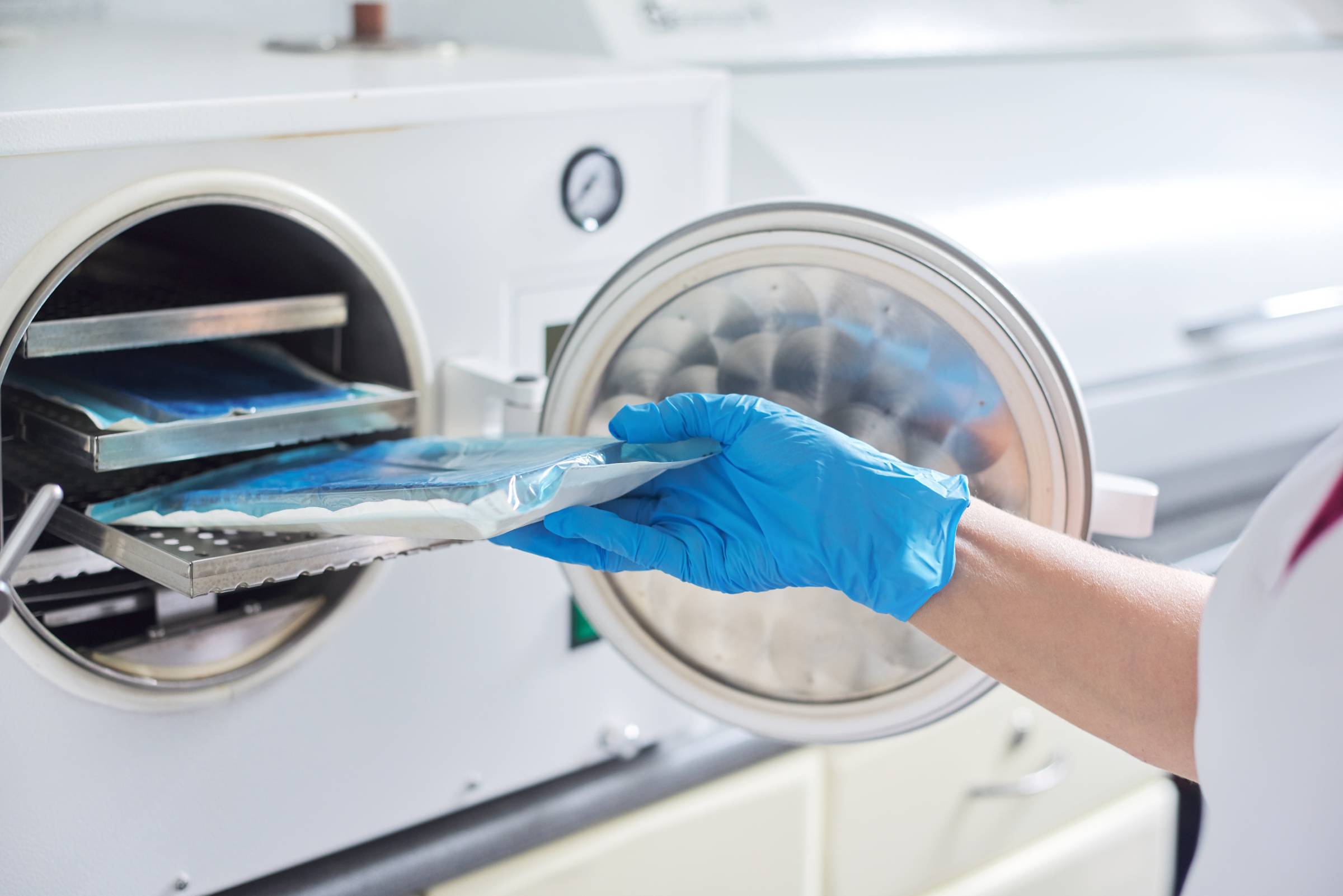 Mensch mit medizinischem Handschuh entnimmt verpackte Instrumente aus einem Sterilisationsgerät.